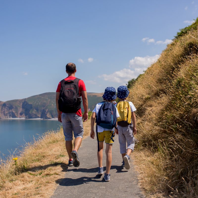 Father and two boys, family walking on a small path along the stunning Devonshire coastline near Lynmouth in Devon, England, UK